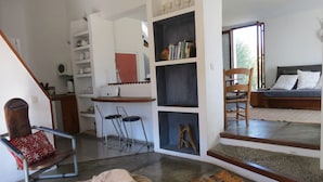 A living room with a sofa, a chair, a bookshelf, and a dining area with a table and chairs. - La Bolina-unique romantic holiday experience, private infinity pool, huge views (torrox)