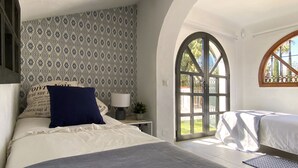 A bedroom with a patterned wallpaper, a bed with a blue pillow, a nightstand with a lamp, and a large arched window. - Chalet in Puerto Marina, Benalmadena Costa. (Benalmádena)