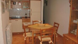 A compact kitchen with a dining table and chairs, a radiator, and a cabinet with glass doors.