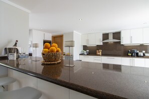 A modern kitchen with a granite countertop, white cabinets, a built-in stove, and a fruit bowl on the island.