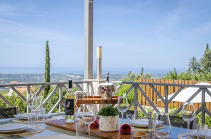 Une table dressée à l’extérieur, avec des verres à vin, une bouteille et une plante en pot, offrant une vue panoramique.