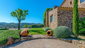 Un edificio de piedra con un camino de piedra que lleva a una zona cubierta de césped, rodeado de vegetación y colinas al fondo.