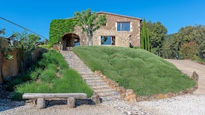 Una casa de piedra con una escalera de piedra que lleva a la entrada, rodeada de vegetación y un cielo azul despejado.