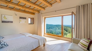 Un dormitorio con dos camas, un ventanal con vistas al campo y vigas de madera en el techo.