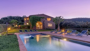 Una casa de piedra con piscina y sillas de descanso.