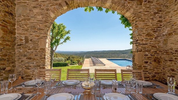 Mesa de comedor lista para seis personas, con vista a una piscina y montañas.