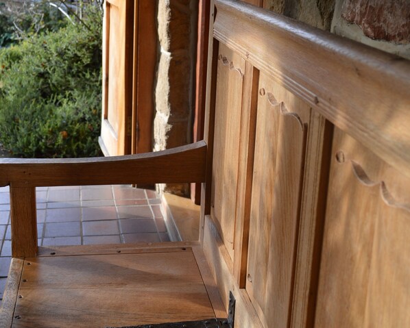A wooden bench with a metal frame, positioned outdoors with a view of greenery and a tiled floor.