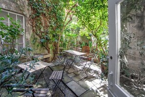 An outdoor patio with tables and chairs, surrounded by greenery and a stone wall.