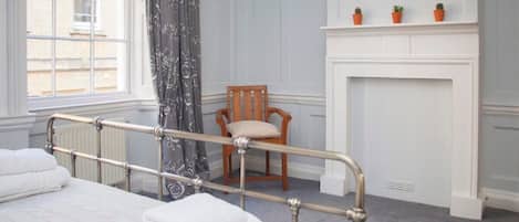 A hotel room with a bed, a chair, a fireplace, and a window with curtains.