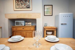 Comedor con una mesa de madera dispuesta para dos personas, un microondas, un refrigerador y un armario de madera.