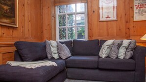 Ein Ecksofa mit passendem Hocker, ein Fenster mit Blick auf Grünflächen und ein gerahmtes Zertifikat an der Wand.