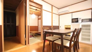 A traditional Japanese-style room with a tatami mat floor, a low table with chairs, a sliding door, and a microwave on a cabinet.