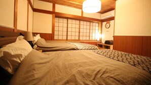A traditional Japanese-style room with two beds, wooden beams on the ceiling, a shoji screen, and a clock on the wall.