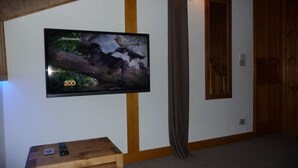 Een flatscreen televisie aan een muur, een houten tafel met een afstandsbediening, en een deur met houten frame.