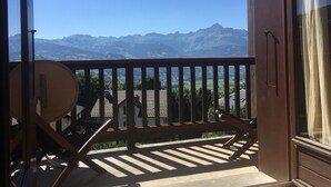 Een balkon met uitzicht op bergen, een houten stoel en een tafel.