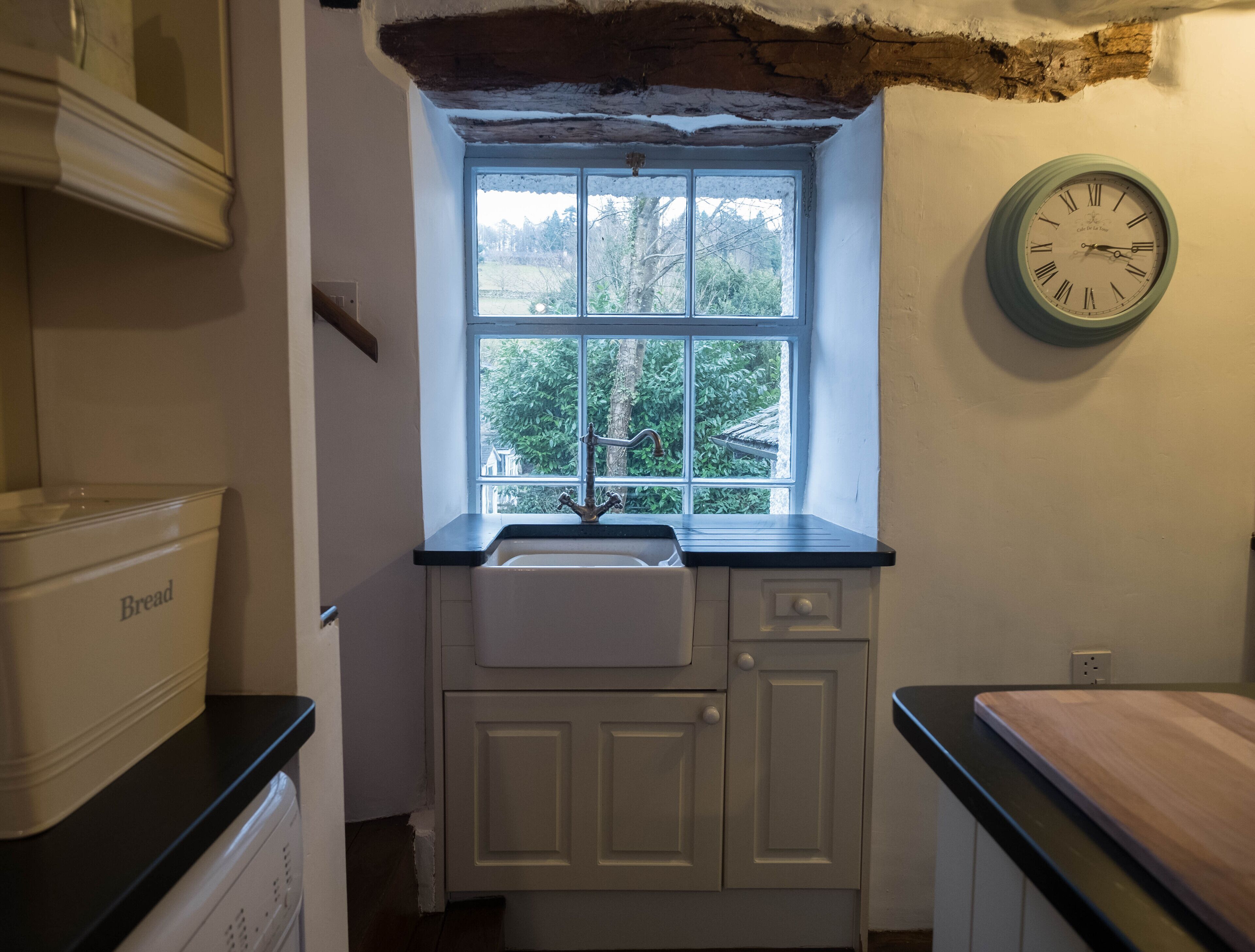 A kitchen with a window, a sink, and a clock on the wall.