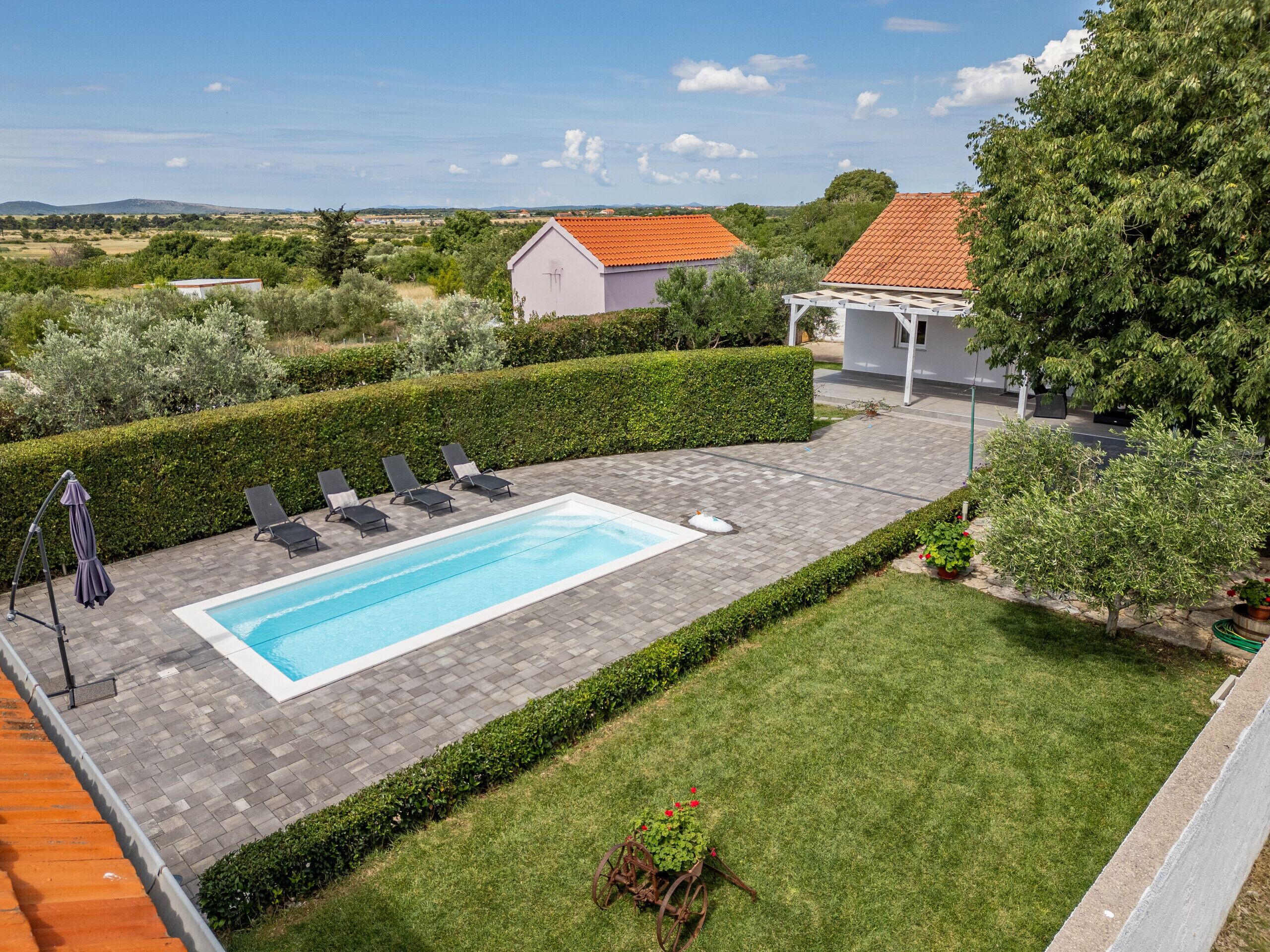 A rectangular swimming pool with a tiled deck, surrounded by a well-maintained lawn and a hedge.