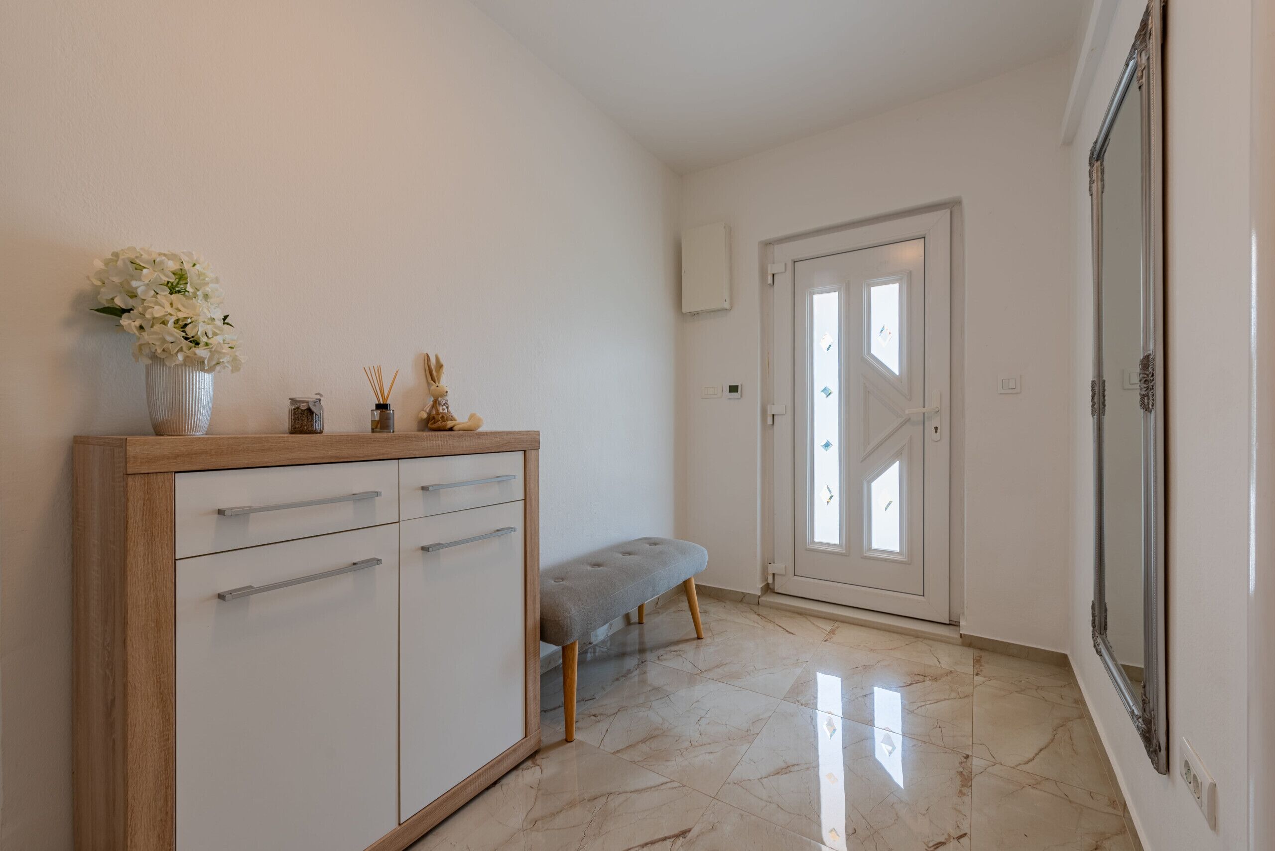 A hallway with a white cabinet, a bench, and a door leading to another room.