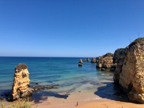 A coastal landscape with clear blue water, rocky formations, and a sandy beach.
