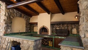 A stone-built outdoor kitchen with a brick oven, a grill, and a tiled counter. - Villa Ciuffo with private pool (Massa Lubrense)