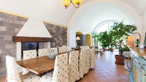 A dining area with a brick wall, a wooden table, and chairs covered with patterned tablecloths. - Villa Ciuffo with private pool (Massa Lubrense)