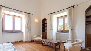 A room with wooden flooring, a bed with a floral bedspread, two chairs, a coffee table, and a bookshelf. - Villa Ciuffo with private pool (Massa Lubrense)