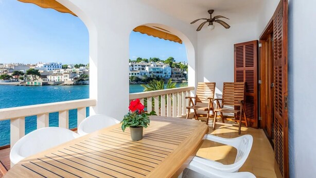 Un balcon avec une table en bois, des chaises blanches et un pot de fleurs.