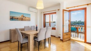 Un coin repas avec une table et des chaises en bois, un tableau au mur et une vue sur la mer par une porte vitrée.