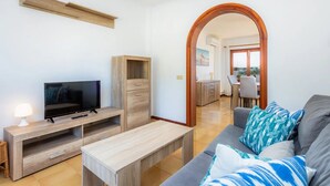 Un salon moderne doté d’un téléviseur à écran plat, de meubles en bois, d’un coin repas avec une table et des chaises, et offrant une vue à travers une arche.