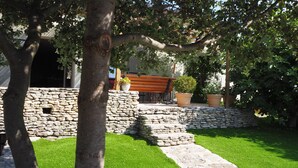 A stone pathway leading to a wooden bench under a tree, surrounded by a stone wall and potted plants. - A cozy home surrounded by nature, with a private pool and tennis court (Cabrières-D'avignon)