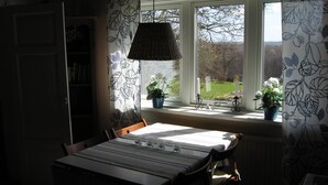A dining area with a table set for four, a window with a view of the outdoors, and two potted plants on the windowsill. - Cozy vacation home for 5 people in Hallandsåsen. (Hjärnarp)