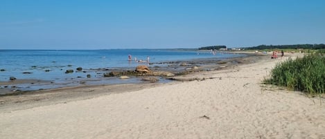 A sandy beach with clear blue water, some rocks, and a few people in the distance.