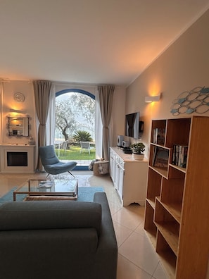 Un salon comprenant un canapé, une table basse, un téléviseur, une bibliothèque et une vue sur l’extérieur.