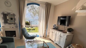 Una sala de estar con un sofá, una mesa de centro de vidrio, un televisor, una chimenea y vistas a un lago.