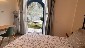 Un dormitorio con cama, escritorio y vista a un jardín por una ventana.