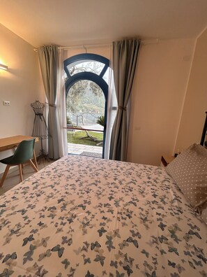 Une chambre à coucher avec un lit, un bureau et une vue sur un jardin, visible par la fenêtre.