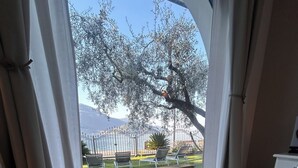 Una habitación con una silla azul, una mesita con una cesta y vistas a un jardín y montañas a través de una ventana.
