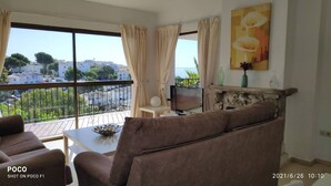 A living room with a sofa, a TV, and a view of a cityscape through large windows. - Enchanting villa with private pool and stunning views, close to beach. (Benalmadena)