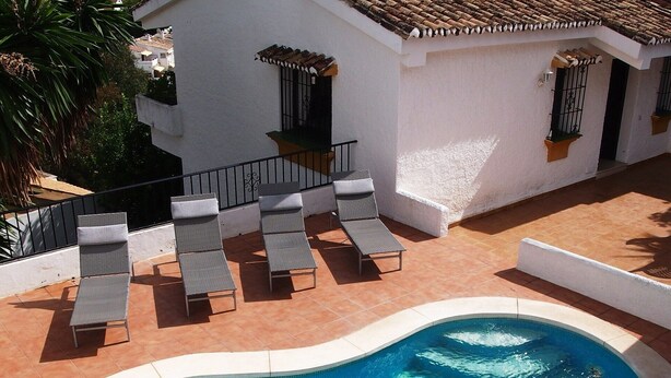 A swimming pool with lounge chairs and a white building with a tiled roof. - Enchanting villa with private pool and stunning views, close to beach. (Benalmadena)