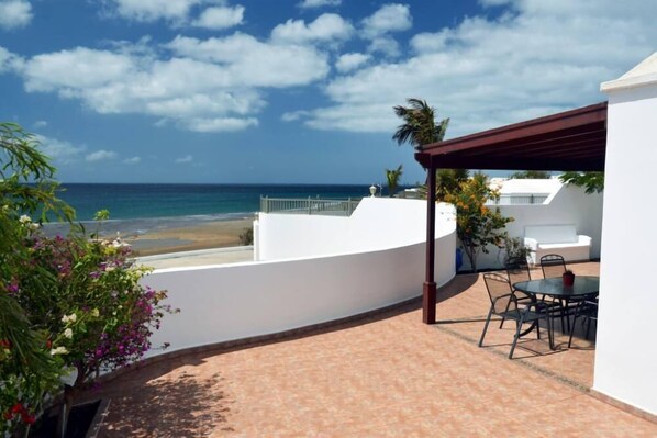 Une terrasse avec vue sur la mer, un espace salon couvert et un bâtiment blanc.