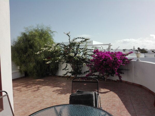 En patio med et rundt bord og stole, en hvid væg og et træ med lyserøde blomster.