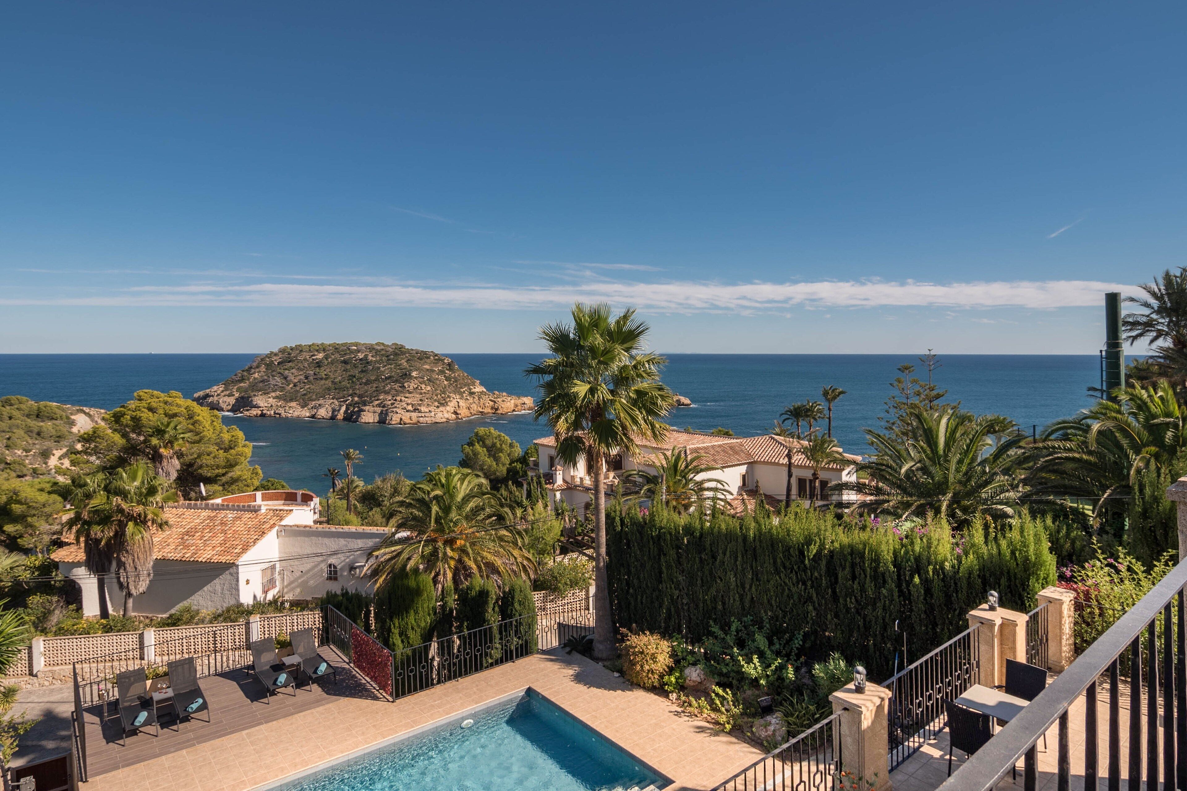 A pool area with lounge chairs, a small pool, and a view of the sea and a rocky island.