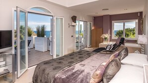 Une chambre avec un grand lit, une télévision et une vue sur la mer, visible à travers des portes vitrées.