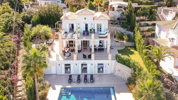 Une maison à deux étages avec une piscine, entourée d’une végétation luxuriante et de palmiers.