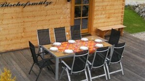 Un comedor al aire libre de madera con una mesa dispuesta para seis personas, rodeada de sillas.
