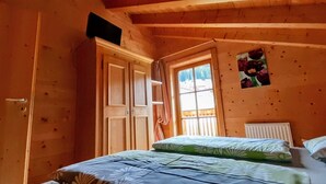 Un dormitorio acogedor con paredes de madera, una cama con ropa de cama floral, una ventana con cortinas y un radiador.