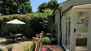 Un espace patio avec une terrasse en bois, une table et des chaises, une plante en pot et une porte vitrée donnant sur une pièce.
