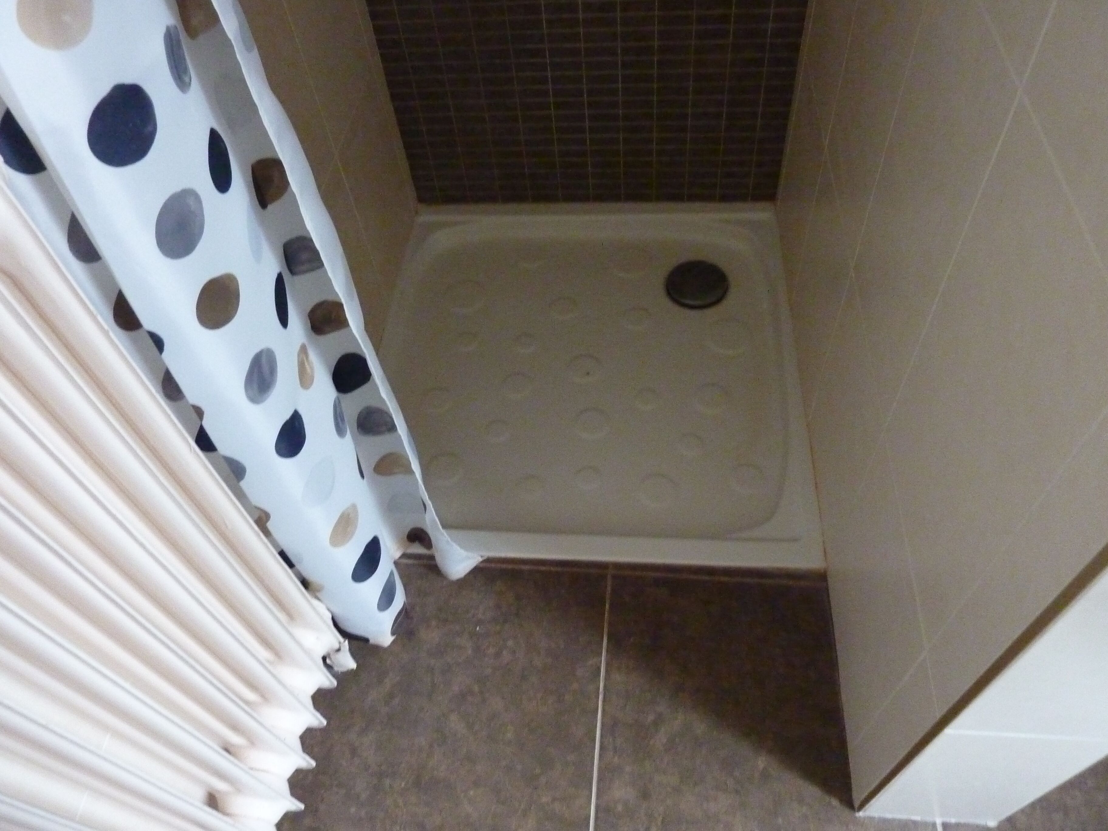 A shower area with a white shower curtain featuring a polka dot pattern, a shower tray with circular grips, and tiled walls.