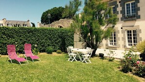 A well-maintained garden with a dining table and chairs, a stone wall, and a large building with multiple windows and balconies. - St Malo F3 62m² Alet Solidor peninsula, sea 50m, wifi, garden, secure parking (ST MALO)