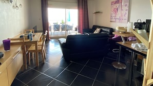 A compact living space with a dining area, a black sofa, and a small kitchen area. - Modern apartment breathtaking sea view and waterfront (Sète)